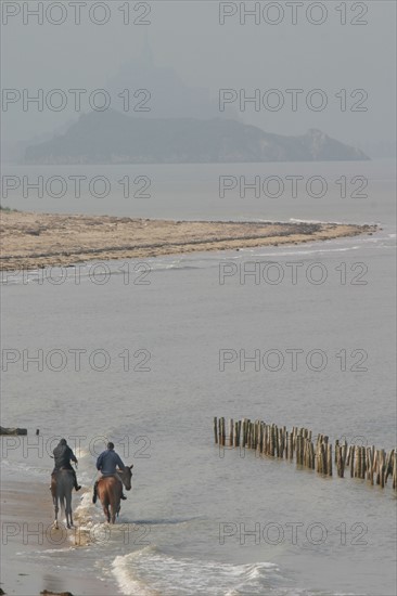 France, Basse Normandie, Manche, baie du Mont-Saint-Michel, cavaliers en trainement chevaux, dragey, mer, vagues, brise maree, rocher tombelaine et Mont-Saint-Michel alignes, brume