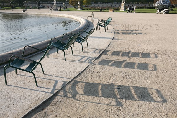 France, Paris 1e, jardin des tuileries, chaises vides et leur ombre allongee pres d'un bassin,