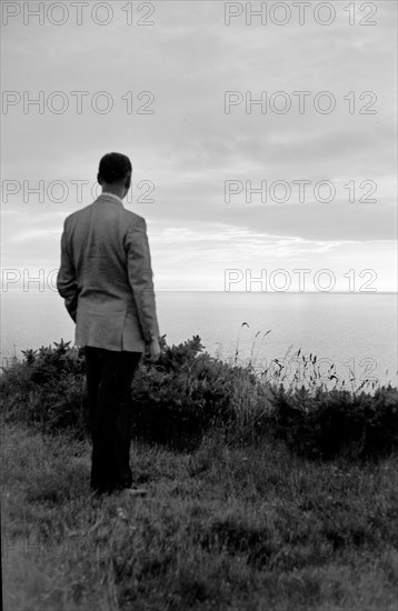 The silhouette of a man standing on a cliff top watching the sunset over the sea, c1945-c1965