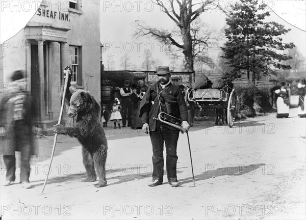 A dancing bear and owner performing outside an inn, Oxfordshire, c1900