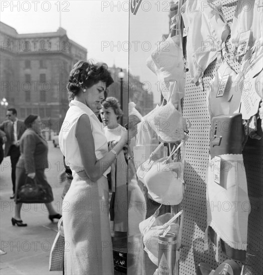 A young woman looking in the window of a lingerie shop in Piccadilly Circus, London, c1946-c1959