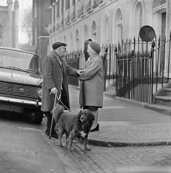 An elderly man chats to an elderly woman on the pavement, London, c1946-c1959