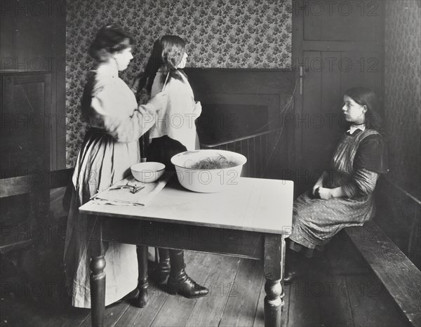 A nurse examines girls' hair, Central Street Cleansing Station, London, 1914. Artist: Unknown.