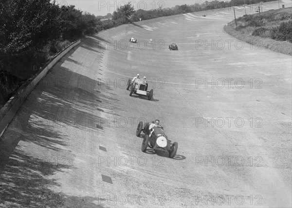 Freddie Dixon's Riley Red Mongrel Special leading RJ Munday's Munday Special, Brooklands, 1933. Artist: Bill Brunell.