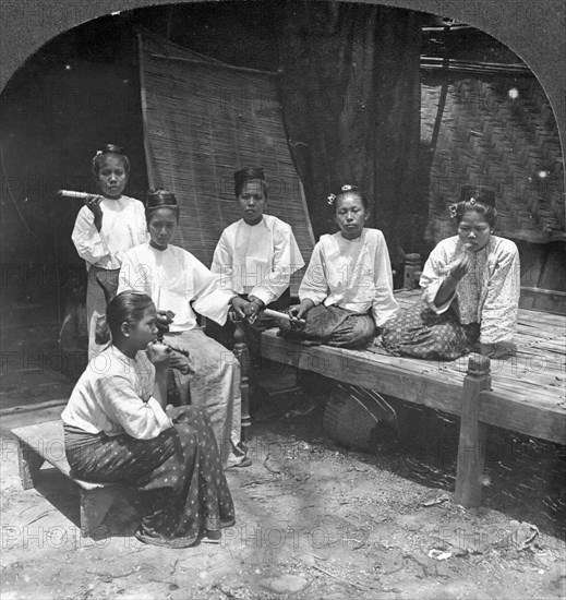 Burmese women smoking outside their home, Mandalay, Burma, 1908.  Artist: Stereo Travel Co