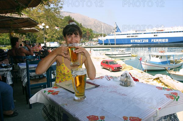 Woman enjoying a drink in a harbourside taverna, Poros, Kefalonia, Greece