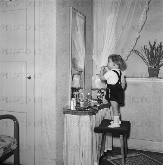 A little girl uses her mother's lipstick in front of a mirror, Sweden. Artist: Unknown