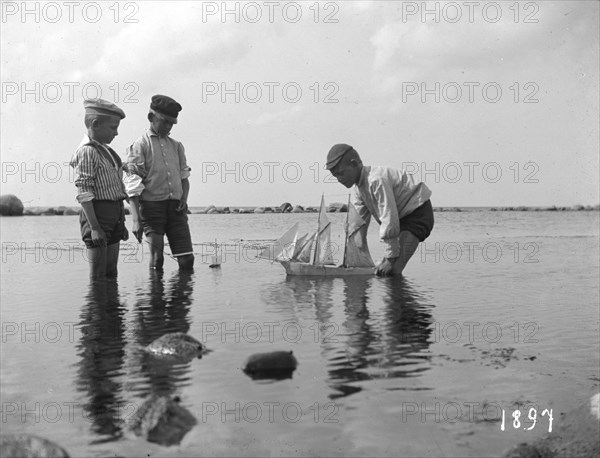 Three boys playing with a model sailing ship, 1897. Artist: Unknown