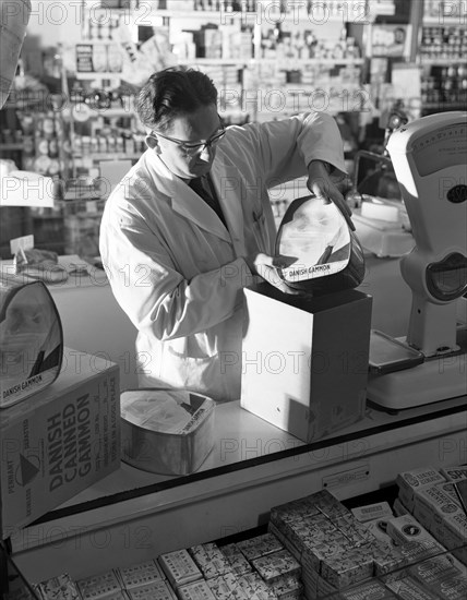 Shopkeeper unpacking canned gammon joints, Mexborough, South Yorkshire, 1963.  Artist: Michael Walters