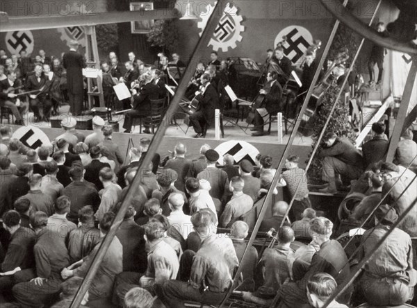 An orchestra plays to some factory workers as they take a break from work, Germany, 1936. Artist: Unknown