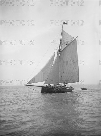 The cutter 'Citara' under sail and towing tender, 1911. Creator: Kirk & Sons of Cowes.