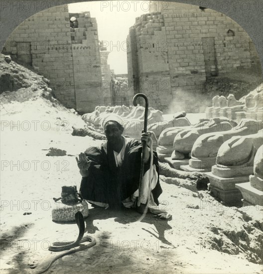 'An Egyptian Snake Charmer Piles His Trade Beside the Avenue of Sphinxes, Temple of Karnak, Thebes,  Creator: Unknown.