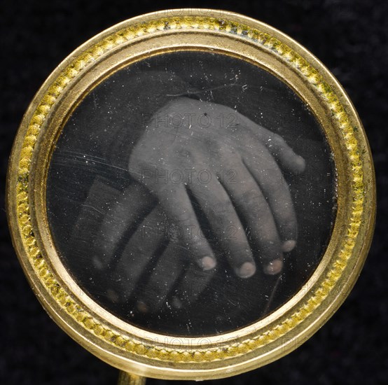 Two hands resting on a book set into a two-piece gold-washed brass frame