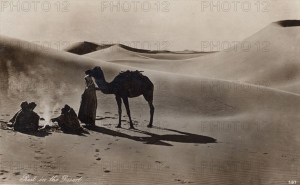 Rest in the Desert, 1930s. Arab men sitting round a campire among sand dunes.
