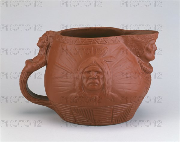 Pitcher, c. 1890.  Earthenware jug with heads of Native Americans on the spout, handle and sides, designed by Edward Kemeys.