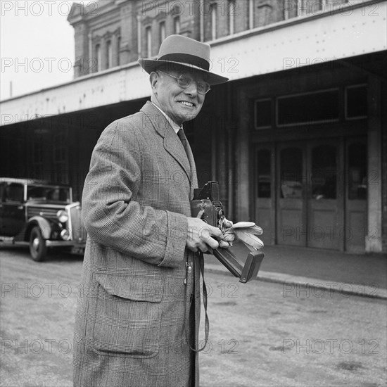 John Laing holding a Rolleiflex camera outside Bournemouth train station, 30/05/1953. Creator: John Laing plc.