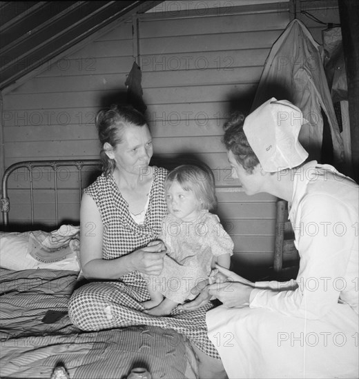 Resident nurse interviews mother and examines sick baby, FSA camp, Farmersville, CA, 1939. Creator: Dorothea Lange.