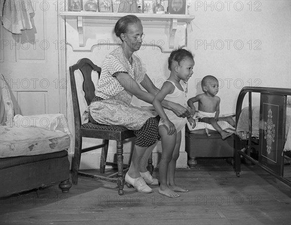 Washington, D.C. Mrs. Ella Watson, a government charwoman dressing her grandchildren.