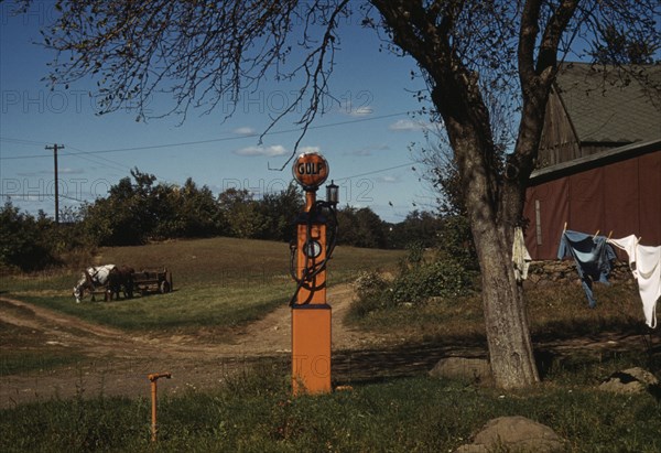 Gas pump with clothesline, barn and horse-drawn wagon in background, between 1941 and 1942. Creator: Unknown.