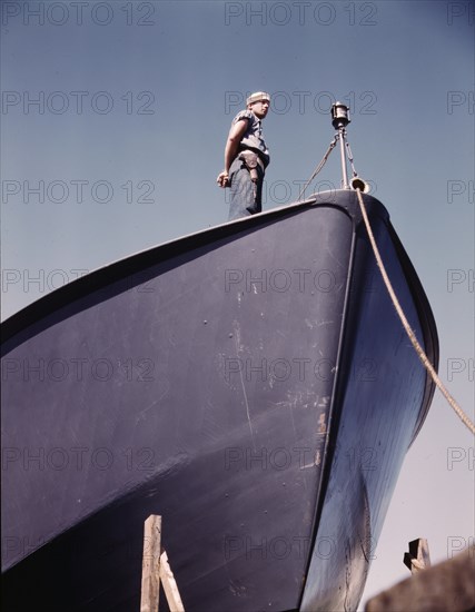 A Coast Guard sentry stands watch over a new torpedo boat under construction at a southern..., 1942. Creator: Howard Hollem.