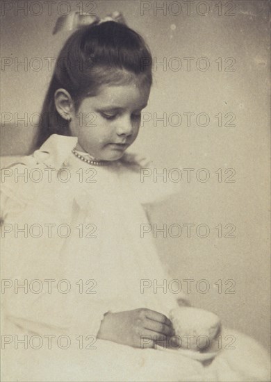 Young girl in white dress, seated holding teacup and saucer, c1900.