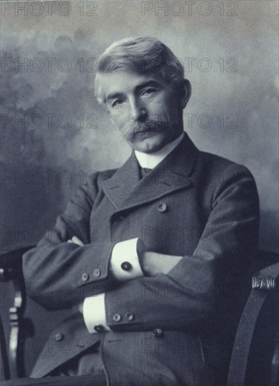 Portrait of man wearing a pinstripe suit seated with his arms crossed, c1900.