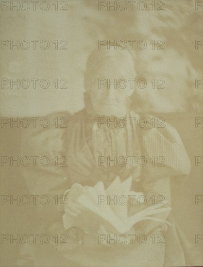 Elderly woman sitting in a chair holding a book, half-length portrait, facing front, c1890.