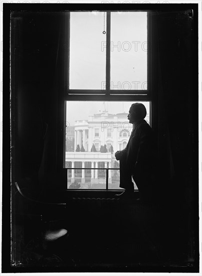 John Skelton Williams at window with White House visible in background, Washington, D.C.