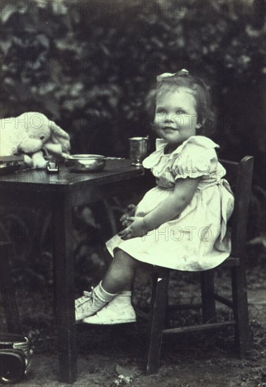 Portrait of a young girl seated at an outdoor table, facing front, between 1940 and 1950.