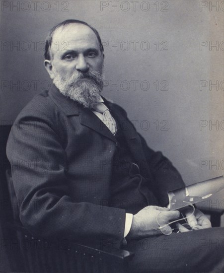 Thomas Hovenden, artist, seated, holding a photograph(?), facing front, half-length portrait, c1895.