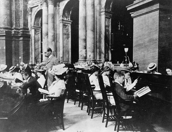 Students in the Reading Room of the Library of Congress with the Librarian of Congress, Herbert Putnam, watching, (1899?).