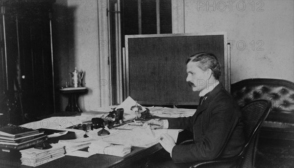 Dr. Miller, Treasury Department employee, half-length portrait, seated at desk, facing left, between 1884 and 1930.