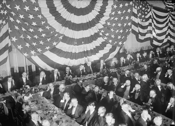 Banquet Scene with Flag Draping And Men Seated Holding Up Listening Device To One Ear, between 1913 and 1917.