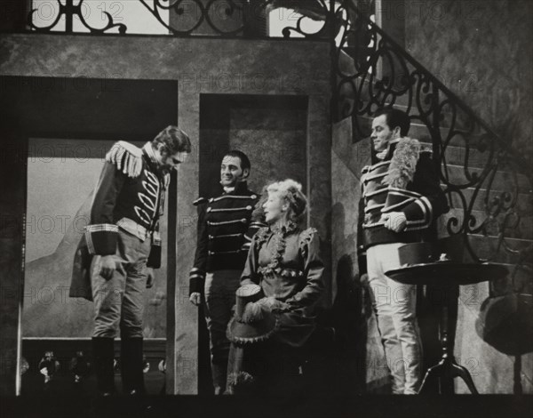 Woman with hat on knee talking to three men, 1938.