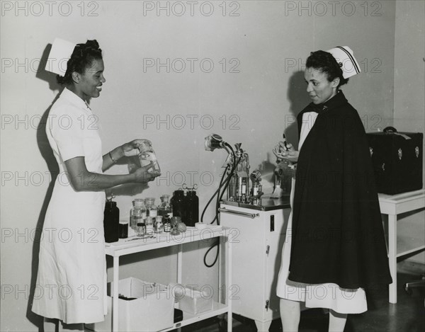 Captain Mary L. Petty, Chief Nurse, holding a glass bottle and showing it to 2nd Lieut..., 1939 - 19 Creator: Unknown.