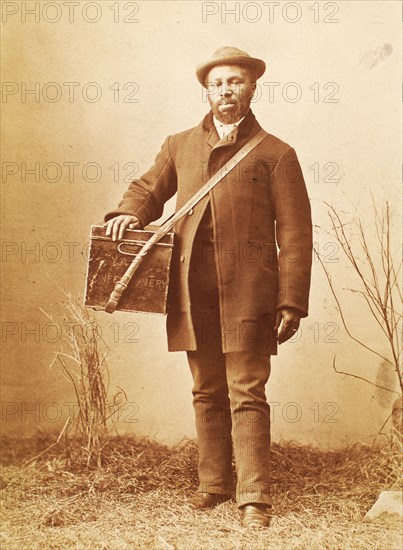 Studio portrait of man holding box labelled 'Confectionery', c1880. Creator: William Notman.