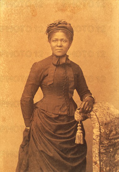 Studio portrait of woman wearing hat and gloves and dress with bustle, c1875. Creator: Unknown.