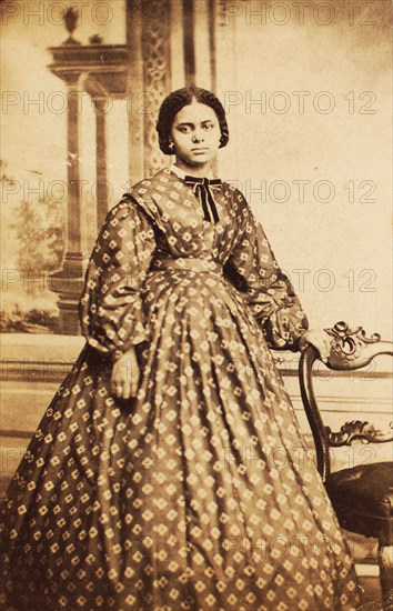 Portrait of young woman wearing patterned dress, with bow at neck, c1860. Creator: Coss & Leach.