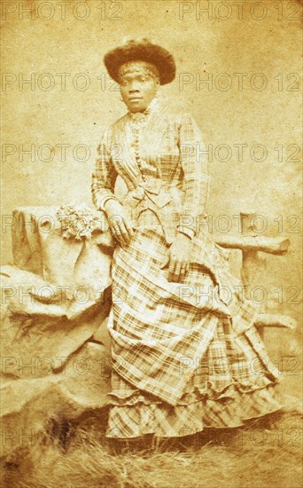 Portrait of unidentified young woman in plaid dress and hat, c1880-c1889. Creator: Thomas Gates.