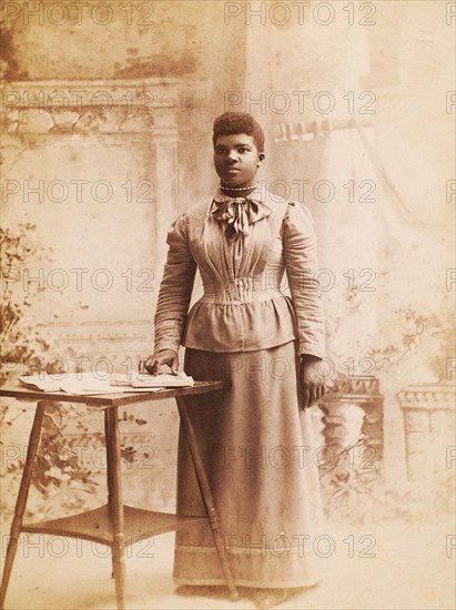 Studio portrait of woman, hand on books spread on table, (1880-1940?). Creator: Madison Art Studio.