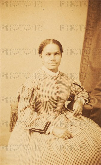 Studio portrait of unidentified seated woman wearing check dress, c1860-c1869. Creator: Decamp & Crane.