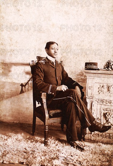 Uniformed man seated, on the mantlepiece is his cap, embroidered with the name...., c1900-c1909. Creator: Roche.