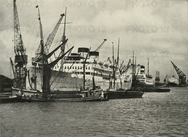 The Forest of Masts Has Given Place to a Cluster of Steamer Funnels Vessels Berthed at...', 1937. Creator: Unknown.