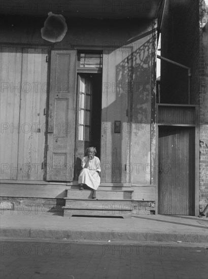 View from across street of a woman sitting on steps, New Orleans, between 1920 and 1926. Creator: Arnold Genthe.