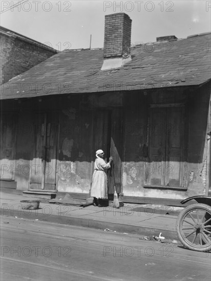 View from across street of a woman with a broom standing in a doorway, New Orleans, c1920-c1926. Creator: Arnold Genthe.