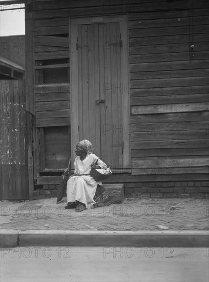 Woman sitting on steps holding a basket, New Orleans, between 1920 and 1926. Creator: Arnold Genthe.