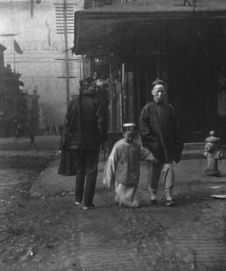 Boy and a man smoking a cigar crossing the street, San Francisco, between 1896 and 1906. Creator: Arnold Genthe.