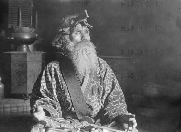 Ainu chief wearing a headdress seated with a sword in his lap, 1908. Creator: Arnold Genthe.