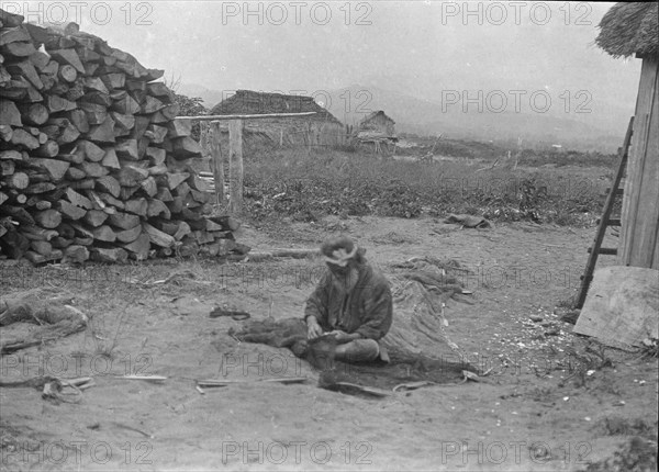 Ainu man seated outside working on nets, 1908. Creator: Arnold Genthe.