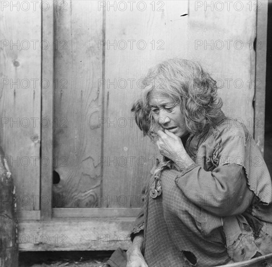 Ainu woman seated by the door of a wooden hut, 1908. Creator: Arnold Genthe.